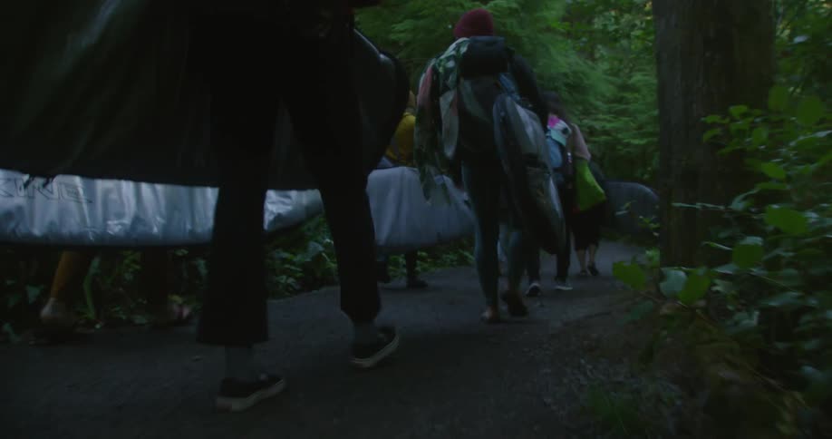 People walk through the forest carrying surfboards