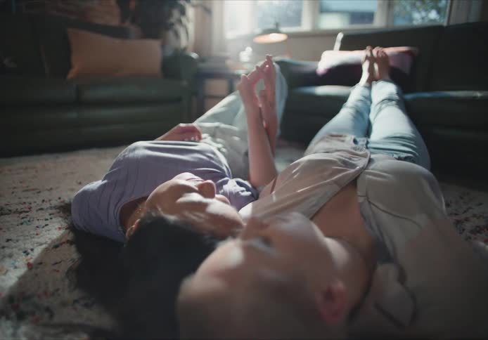 Young couple holding hands while laying on the floor of the living room together with their feet up the couch