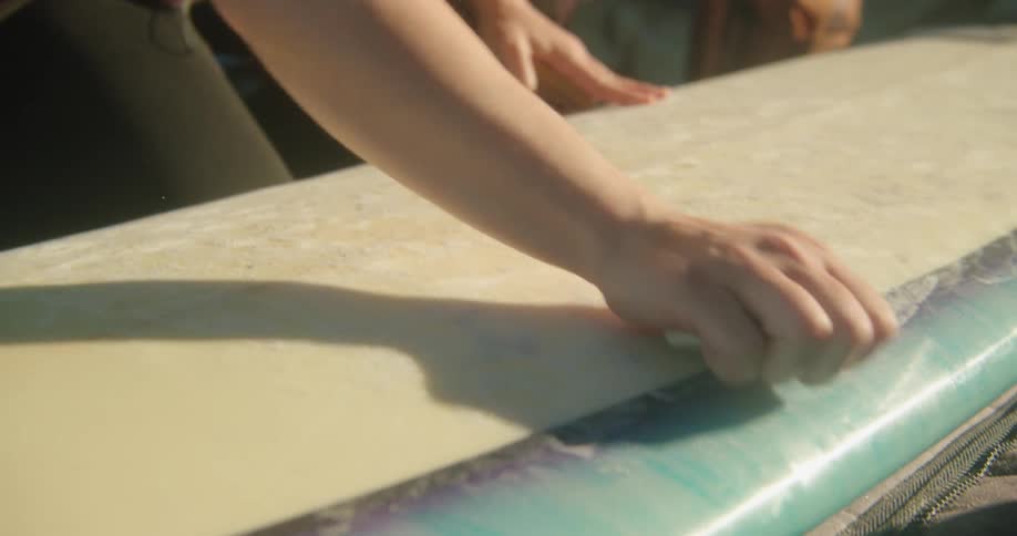 A surfer rubs wax over their surfboard