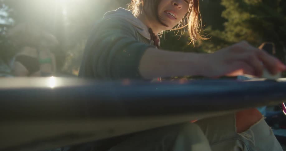A woman looks up smiling and talking as she waxes a surfboard