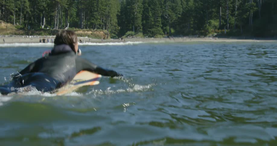 A woman lays on a surfboard and paddles toward the shore