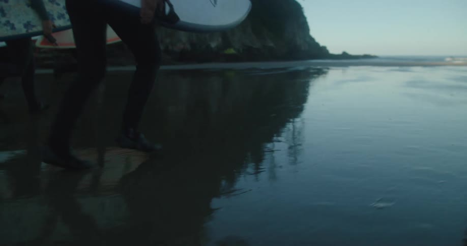 A group of surfers run across wet sand carrying their boards toward the ocean