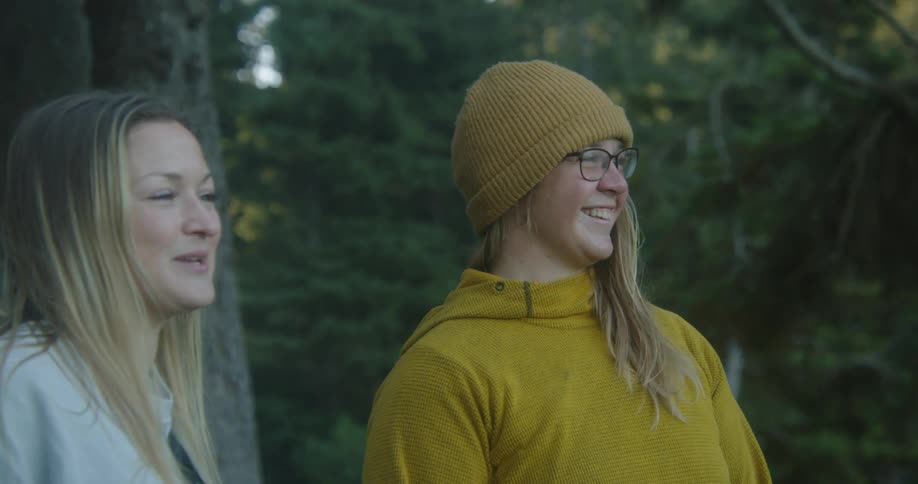 Two teenage girls are standing near trees talking and laughing