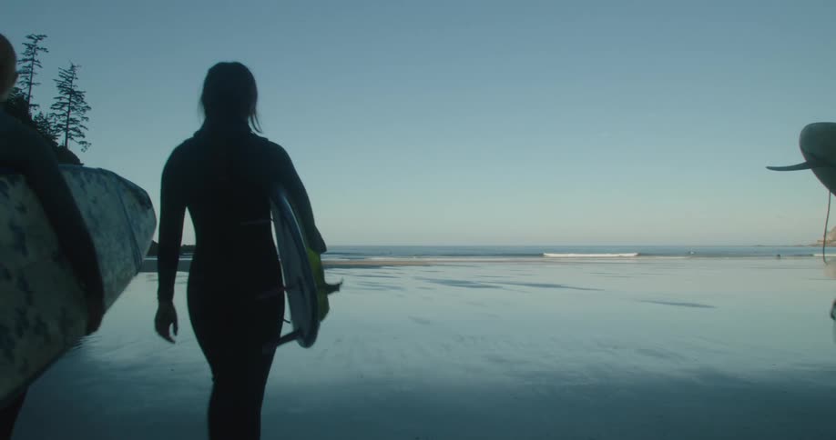 A group of women walk to the water edge with surf boards