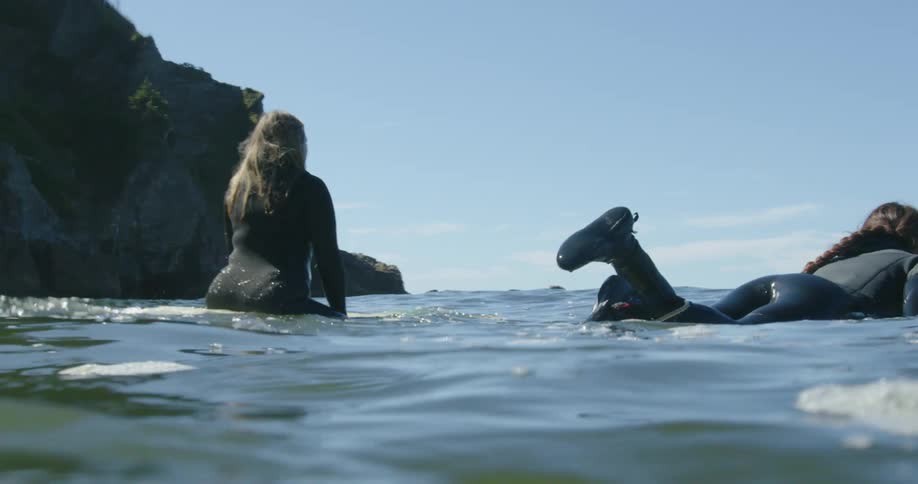 Women surf out past the rocky shore