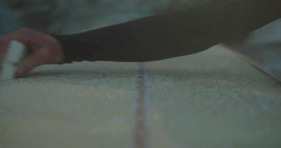 Person wearing wet suit waxes surfboard