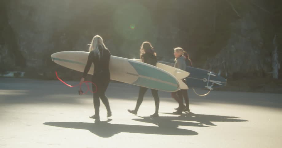 Four women are walking on the beach with surfboards