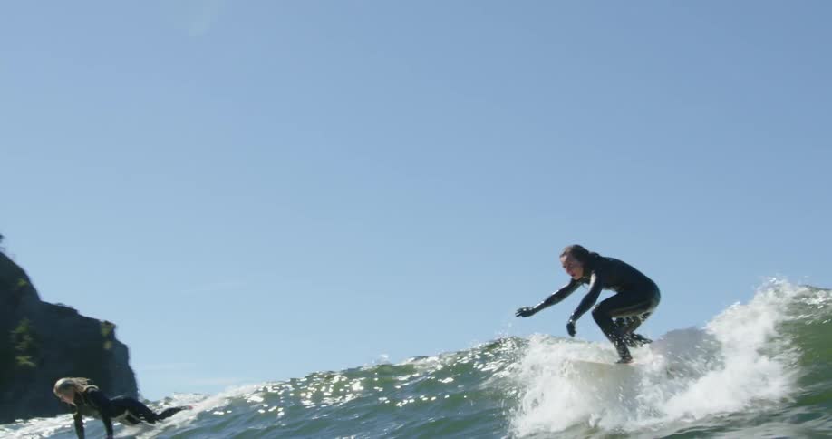 Two women jump on their surfboards to catch an incoming wave