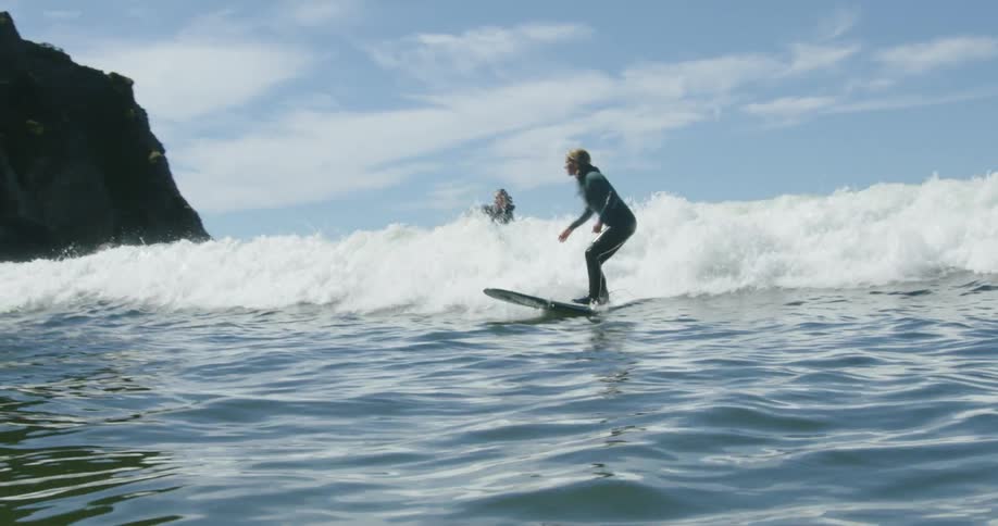 A group of surfers with wetsuits rides sea wave next to cliff