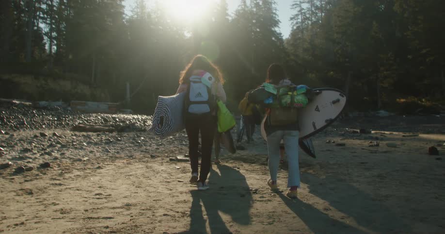 A group of women carry their surfing equipment away from the beach on a sunny day