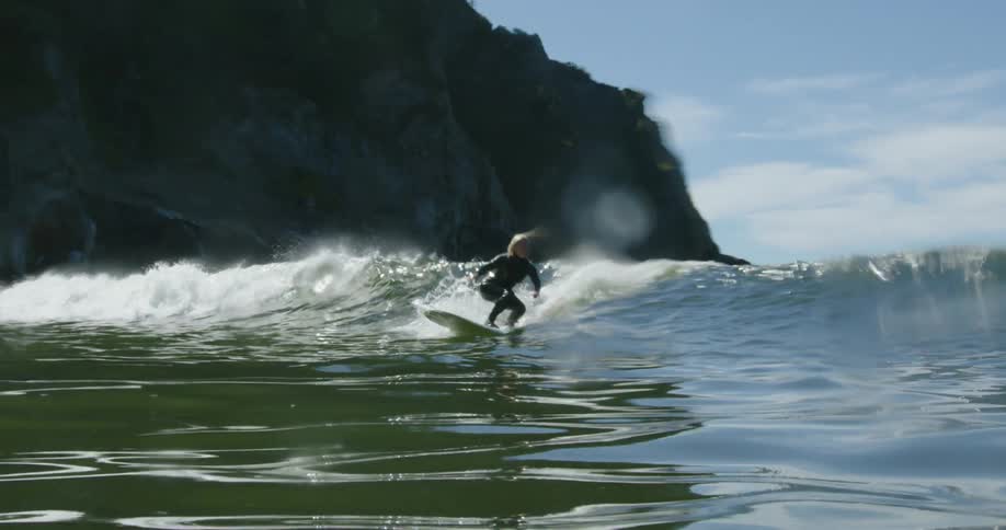 A woman stands up on a surfboard to ride the incoming wave