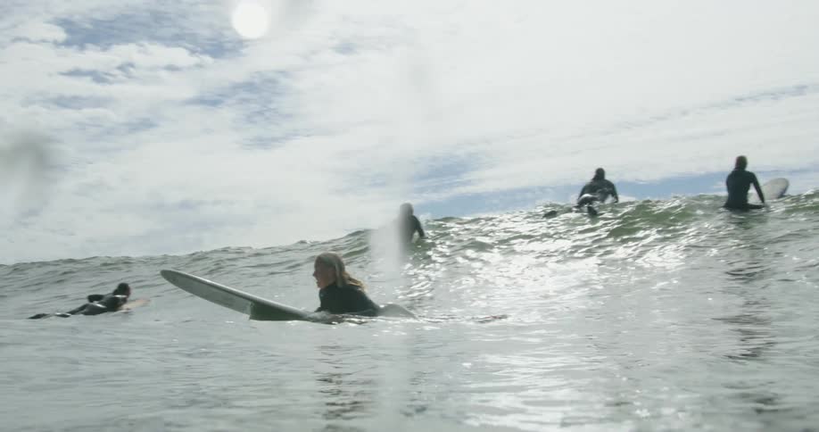 A surfer paddles with her hands while lying on her stomach atop her surfboard on the ocean during the day