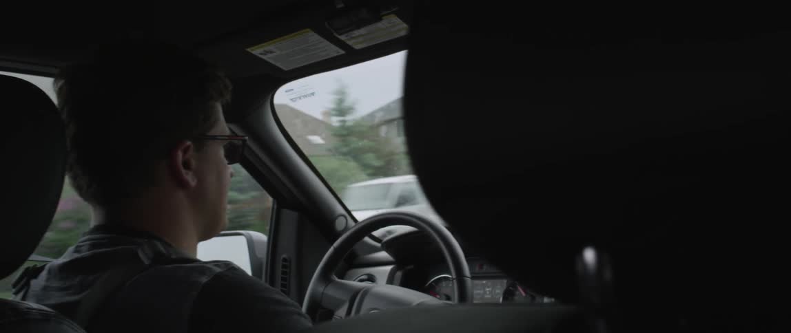 A man is driving a car past homes
