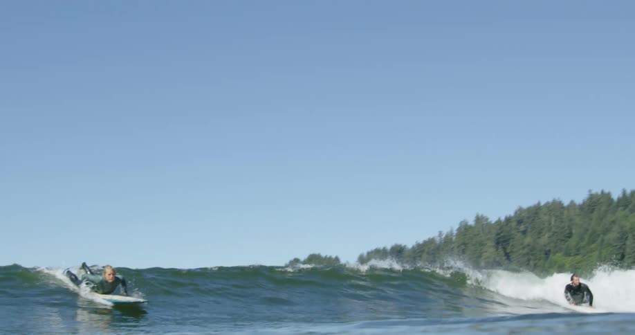 A surfer stands up on her surfboard as an ocean wave catches up to her