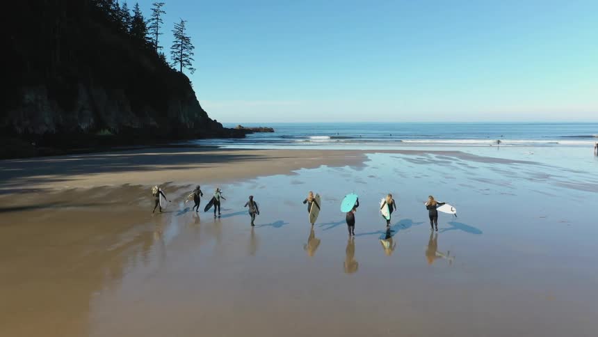 A group of women with surfboards run from the beach out to the water