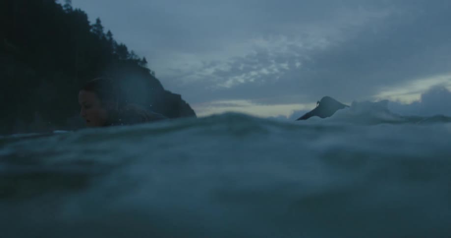 A woman in a full wet suit is surfing on choppy waves