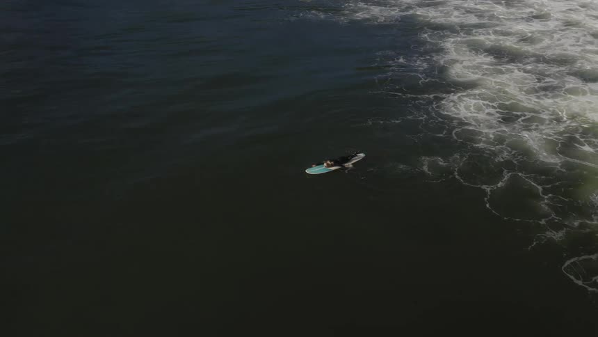 Woman wearing a black wet suit swimming over a surfboard in the ocean waiting for waves