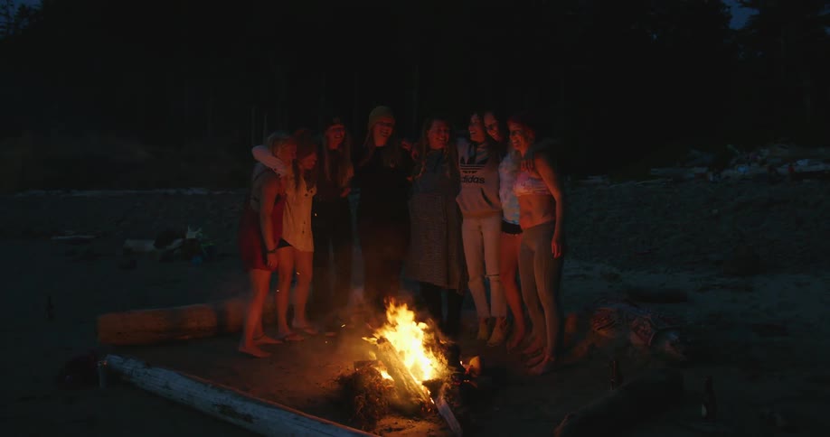 Group of young girls standing around a bonfire at the beach at nigt