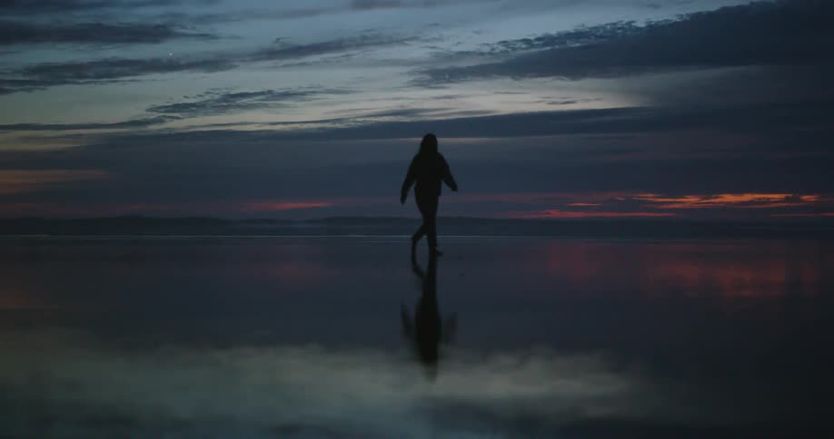 Silhouette of a person walking over wet sand on the coast at sunset