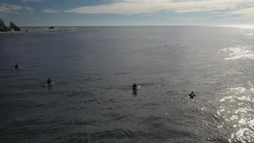 A group of surfers sit atop their surfboards on the ocean during the day