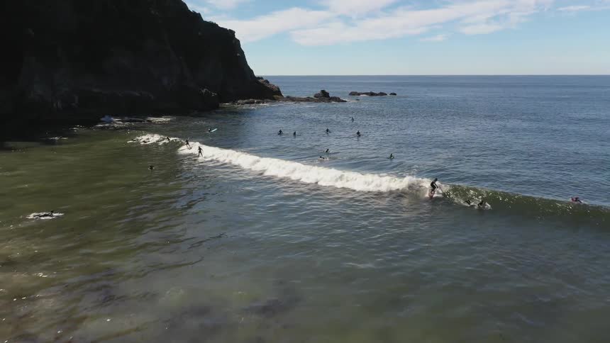 Swimmers and surfers play in the ocean at a beach during the day