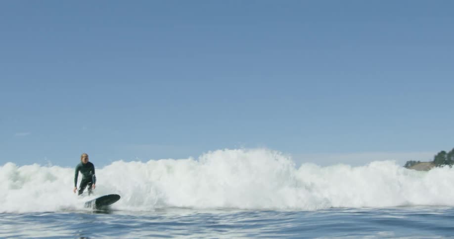 Blonde woman surfs crashing wave on lightly cloudy day