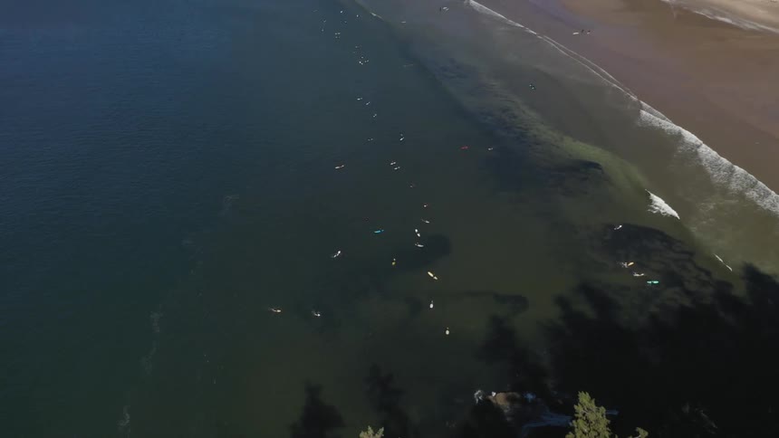 Aerial view of a beach and many people in the water on surfboards