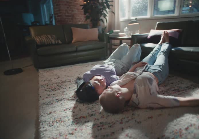 A woman rests her head on the shoulder of a woman lying beside her on rug in a living room during the day