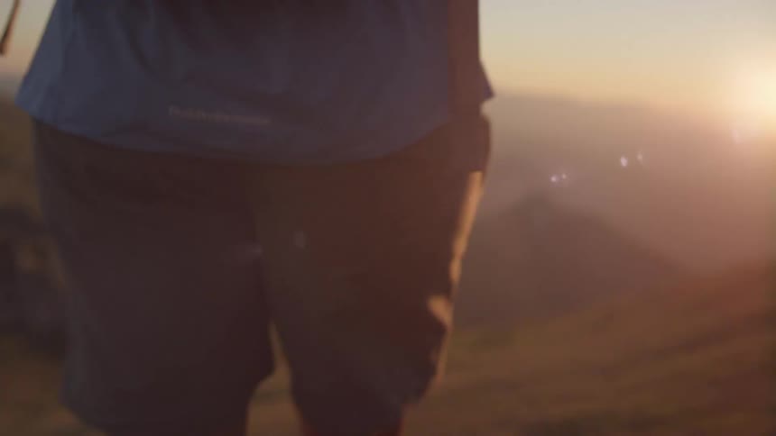 A person carrying a backpack walks on the slopes of a mountain at sunset
