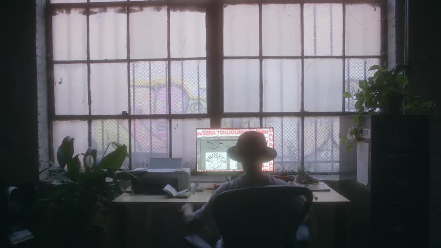 A man walks into a room and sits at a computer desk