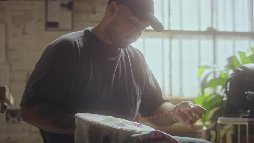 A man sitting embroidering fabric using a hoop and needle