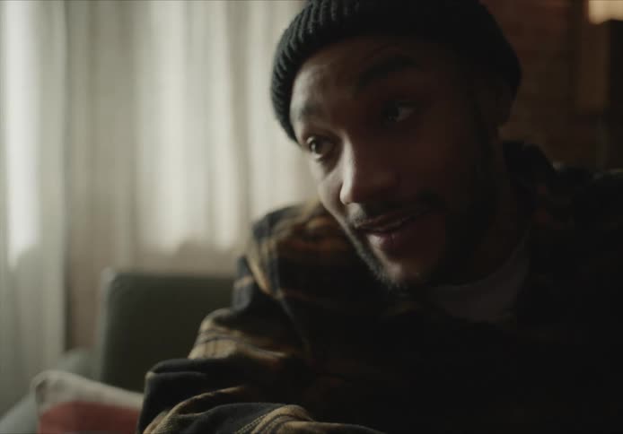 A man speaks animatedly while sitting inside in a coat and hat