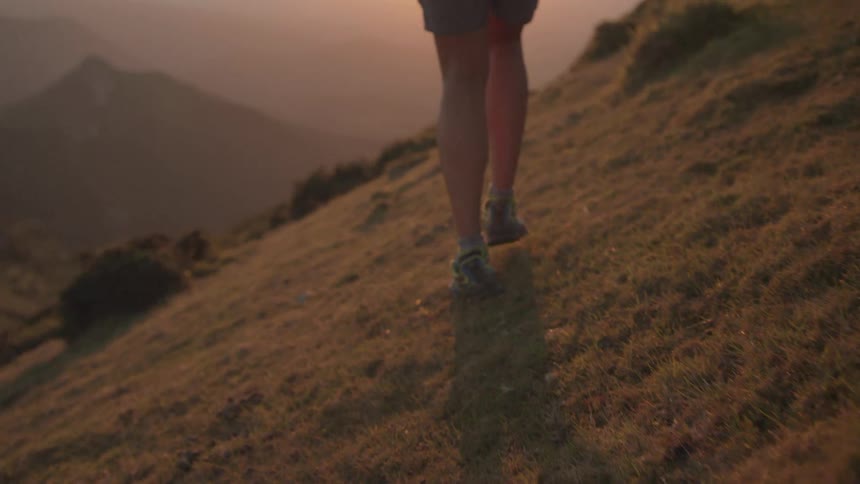 Man wearing shorts walking on the slope of a mountain at sunset