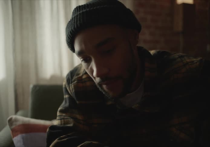 Man wearing a beanie sitting on a dimly lit living room at home