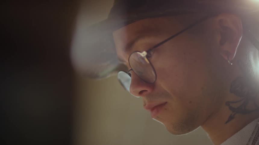 Young man wearing glasses and a hat with a tattoo on his neck