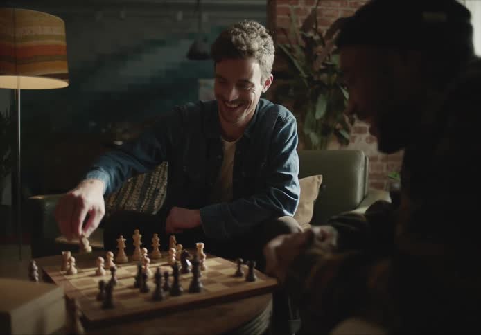 Two men sitting in armchairs play chess talking and laughing