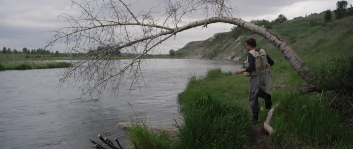 Man with fishing pole walking towards edge of lake