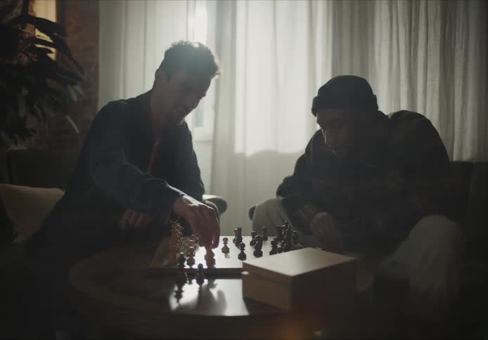 Two friends are sitting indoors and playing a game of chess