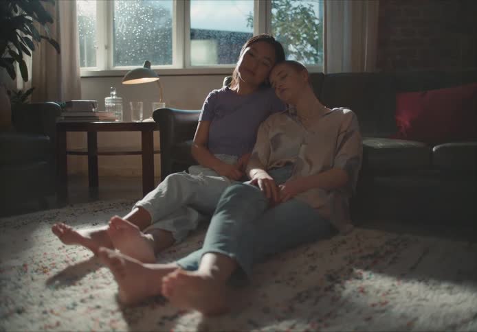 A woman puts her head on her girlfriends shoulder as they relax on the floor