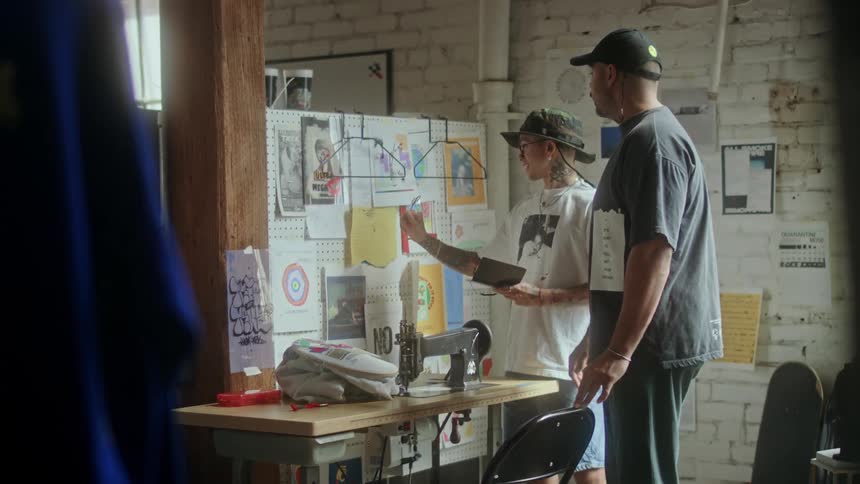 Two men talk together in front of a bulletin board in a workshop