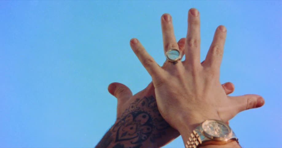Tattooed male hand and female hand with a wristwatch and ring extended in the air against the blue sky