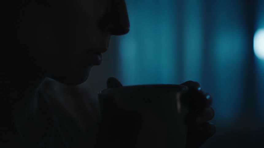 A woman blows in to a mug containing a hot beverage