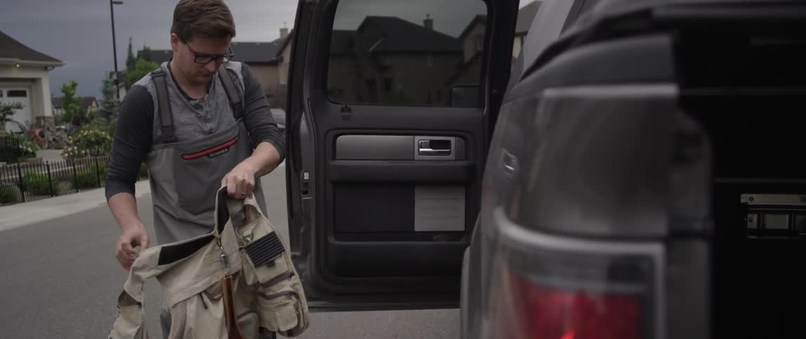 A man removes a vest from his truck and wears it