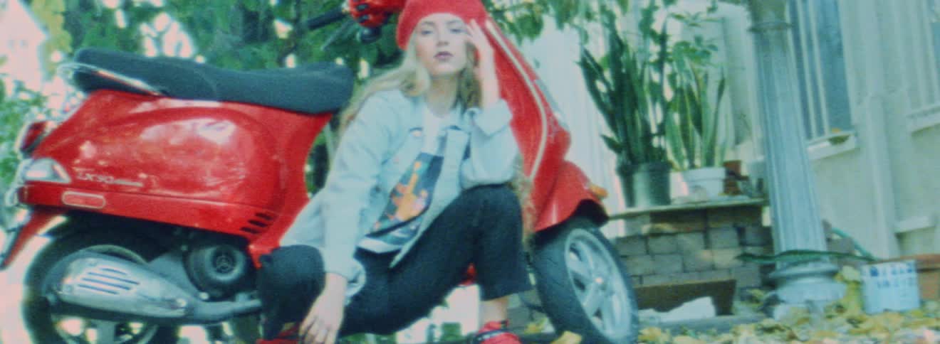 A woman poses as she squats down in front of a moped