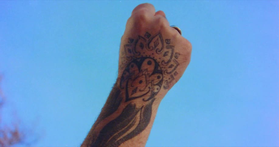 Man raises tattooed fist up in the blue sky