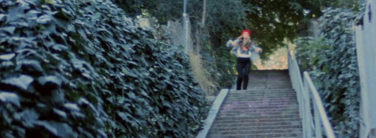 Blonde female dancer wearing a red beret dances on outdoor staircase bordered by ivy