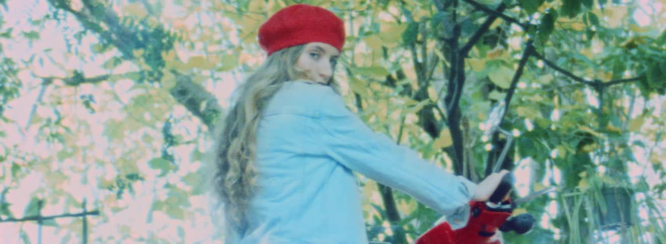 Blonde woman wearing denim jacket and red hat modeling for the camera in front of trees
