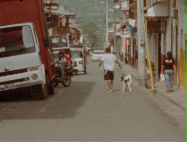 Man walking a dog down the street of a small town caught on vintage film