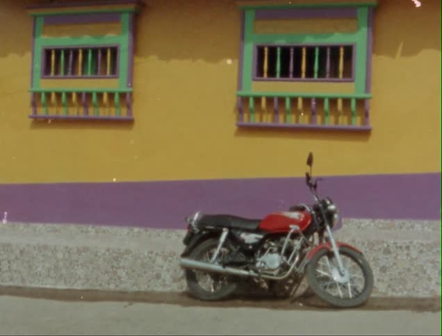 Red motorcycle parked against the colorful wall of a house caught on vintage film
