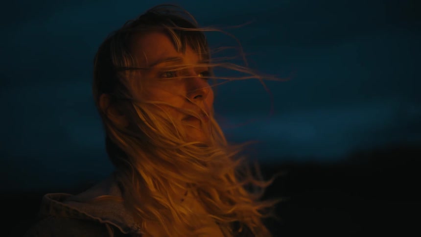 A woman stands outside at night and closes her eyes as the wind blows through her hair
